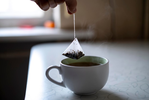 La main d'une personne tenant un sachet de thé et faisant une tasse de thé chaud