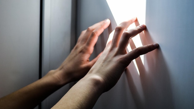 La main d'une personne touche un mur blanc avec la lumière qui brille dessus.