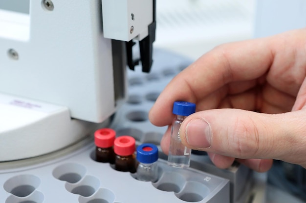 Main de personnes tenant un ensemble de flacons de tubes à essai pour analyse dans le chromatographe gaz-liquide Assistant de laboratoire insérant une bouteille en verre de laboratoire dans un flacon de chromatographe