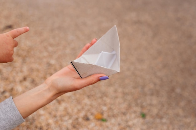 Main avec petit bateau en papier à partir de papier sur le sable près des vagues de la mer Concept bateau en papier sur une plage de sable près de la mer en automne ou en journée ensoleillée Voyage tourisme vacances repos vacances