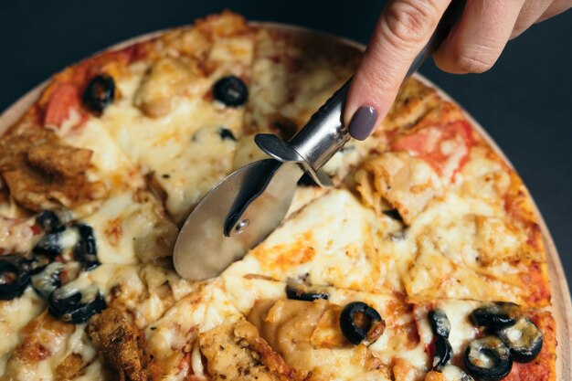 Main de plan rapproché de boulanger de chef dans la pizza de coupe uniforme blanche à la cuisine