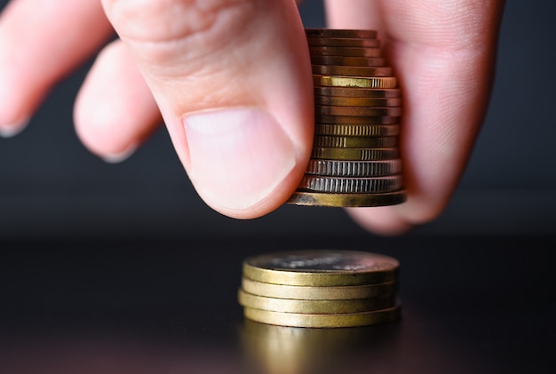 La main plie une tour de pièces de métal sur fond noir.