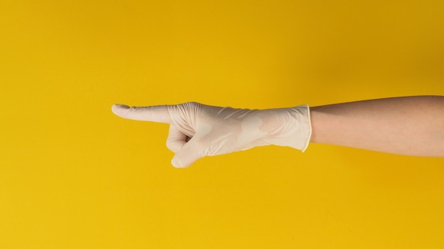 La main pointe le doigt et porte un gant médical sur fond jaune. Tournage en studio.