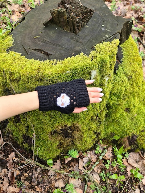 Une main portant un gant tricoté noir avec une fleur blanche dessus.