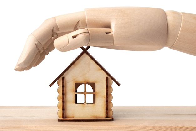 La main de la poupée en bois couvre une maison de jouet en bois isolée sur blanc Concept de protection d'assurance