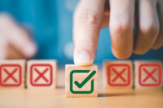 Main poussant le symbole vert correct devant le signe de la Croix-Rouge sur un cube en bois pour la proposition commerciale et le concept d'approbation de document