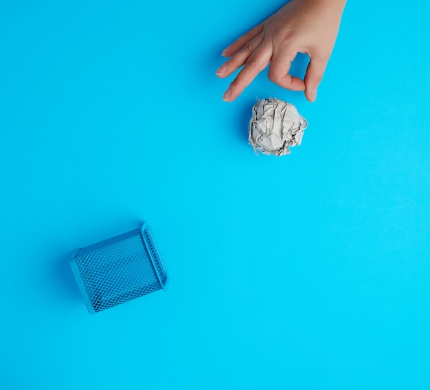 Main a poussé une boule de papier gris froissé dans une poubelle en métal