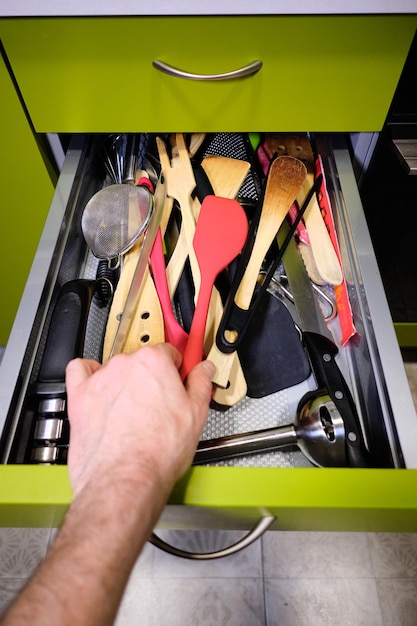 Photo main prenant une cuillère en bois à l'intérieur d'un tiroir de cuisine plein de couteaux et d'ustensiles de cuisine