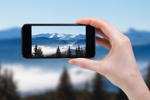 Main prenant une photo des sommets des montagnes avec téléphone portable