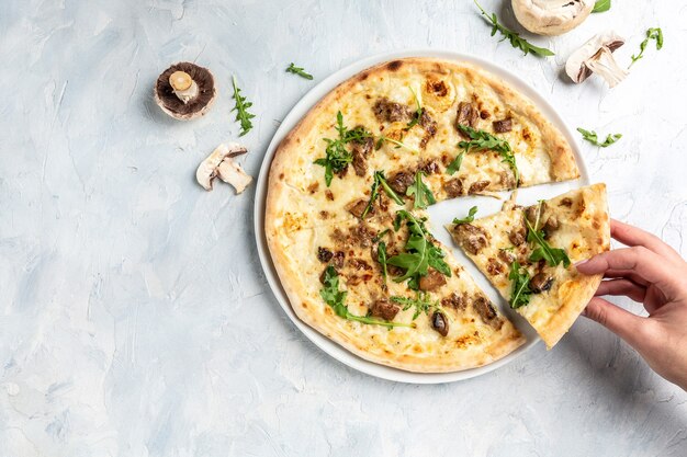 Main prenant des tranches de pizza avec mozzarella, champignons et roquette. Pizza italienne. bannière, menu, lieu de recette pour le texte, vue de dessus.