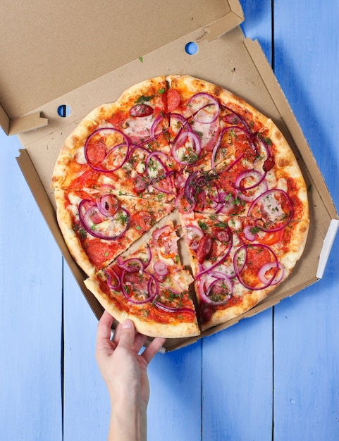 La main prend un morceau de pizza en boîte sur table en béton bleu