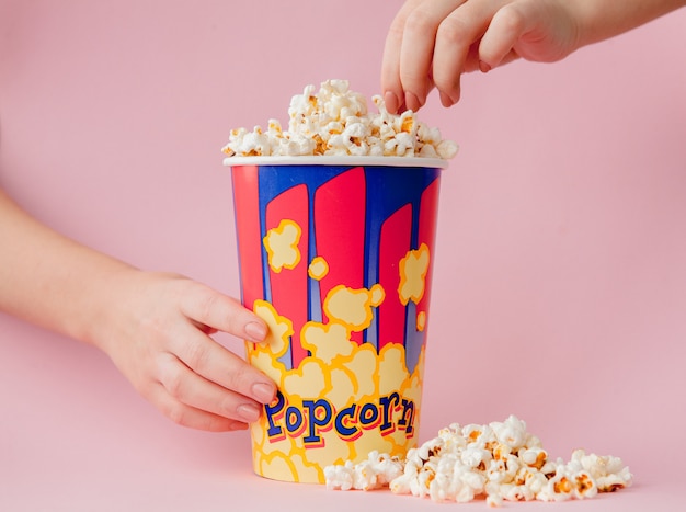 Main prend un pop-corn dans un gobelet en papier