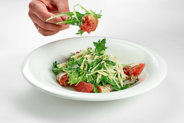 La main prend une salade d'anguille et de pamplemousse d'une assiette blanche sur une nappe blanche Mise au point sélective en gros plan