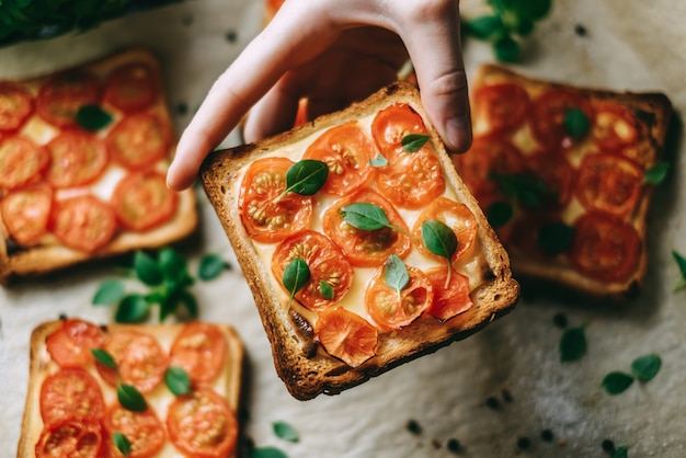 La main prend un sandwich cuit au four avec du fromage et des tomates cerises sur du pain noir.