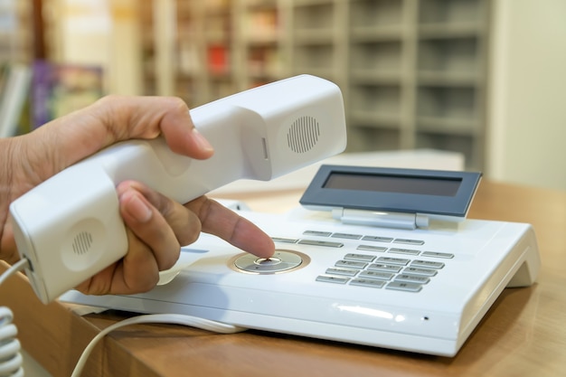 La main prend le téléphone et appuie sur le bouton du téléphone de bureau ou de l'ancien téléphone.