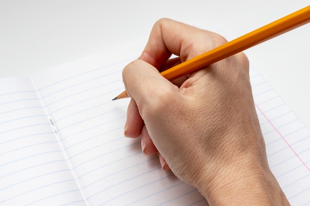 Main qui écrit sur une feuille de cahier lignée blanche avec un crayon jaune