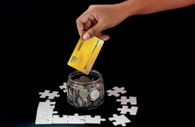 La main qui a ramassé la carte de crédit et les pièces du puzzle et la tirelire sur fond noir avec des espaces pour le texte