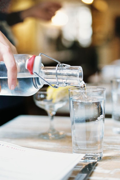 Une main qui verse de l'eau d'une bouteille avec un clip dans un verre