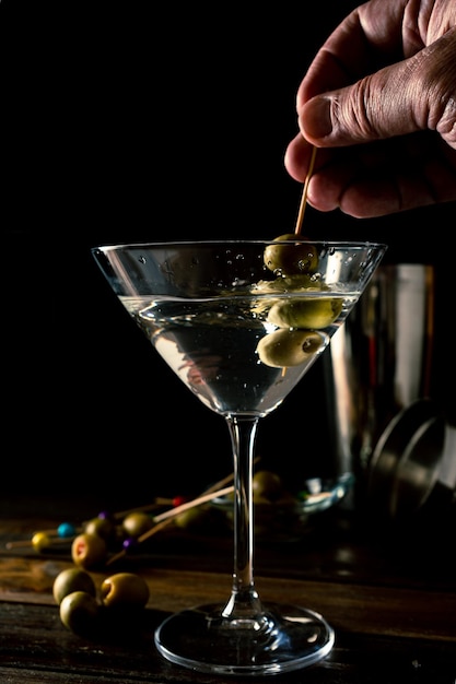 Une main retirant des olives d'un verre à martini conique classique et générant des éclaboussures. Orientation verticale.