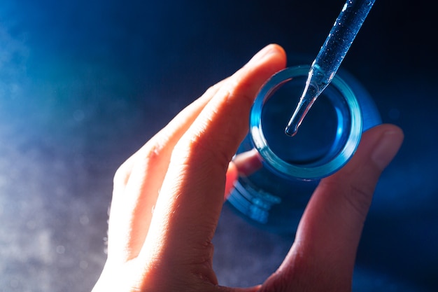 La main d'un scientifique tenant un flacon avec des ustensiles de laboratoire et des tubes à essai dans le fond d'un laboratoire chimique