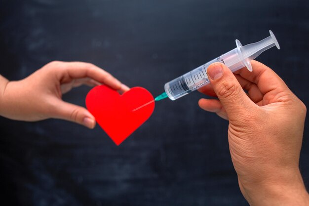 Une main avec une seringue jetable fait une injection dans le symbole du coeur