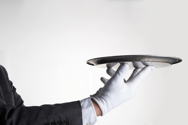 Main de serveur élégant dans un gant blanc tenant une assiette vide avec un fond blanc