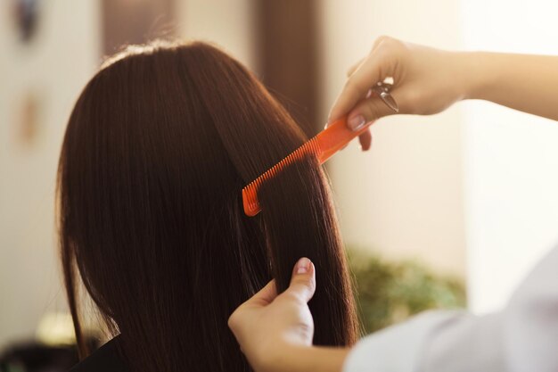 Main de styliste avec peigne peignant les cheveux de la femme au salon