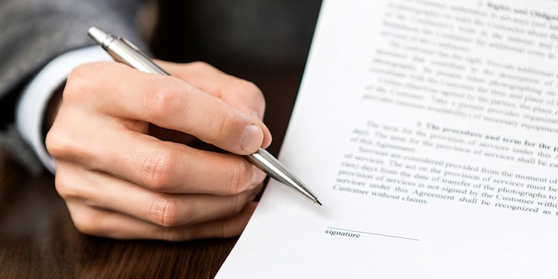 La main avec le stylo à bille argenté indique un espace vide pour la signature.