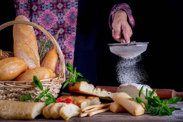 Main tamiser la farine sur un pain dans une table en bois avec une variété de pains