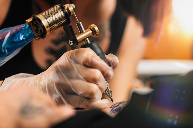 Main de tatoueur dans des gants en caoutchouc dessinant un tatouage avec un gros plan de pistolet de tatouage électrique
