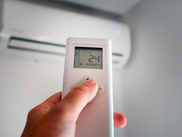 Main avec télécommande et réglage de la température du climatiseur sur un mur blanc