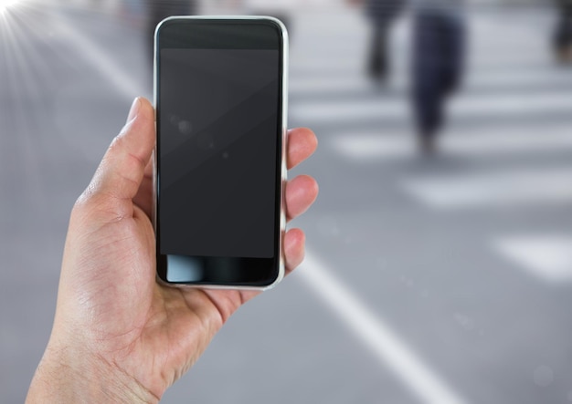 Main avec téléphone contre rue floue avec flare