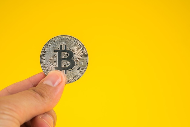 Main tenant Bitcoin entre les doigts sur fond jaune.