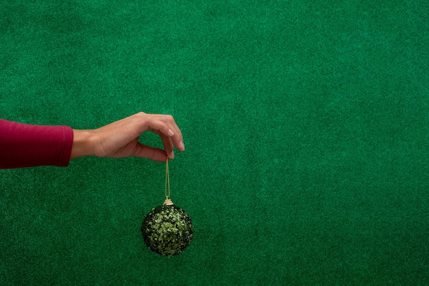 Main tenant une boule verte de Noël sur fond vert