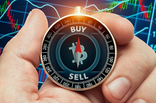 Photo main tenant une boussole avec un symbole de trésorerie bitcoin brillant et devant les données du graphique boursier