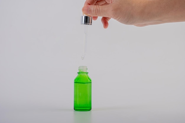 Photo la main tenant une bouteille de goutte-à-goutte en verre vert sur fond blanc