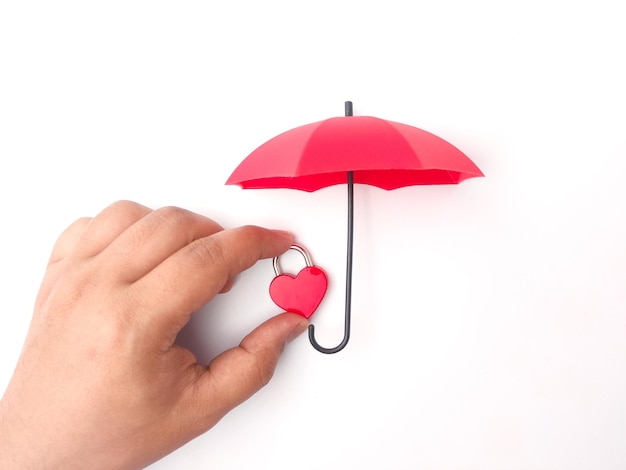 Main tenant un cadenas d'amour rouge protégé par un parapluie rouge sur fond blanc