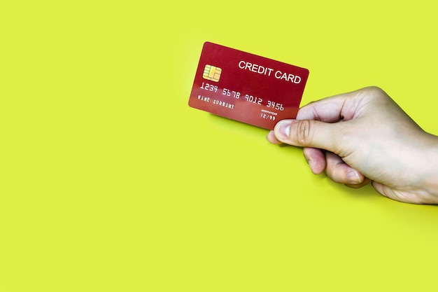 Main tenant une carte de crédit rouge sur fond jaune, la carte de crédit peut être utilisée pour payer des biens ou des services, concept de carte de crédit. Tracé de détourage de carte de crédit.