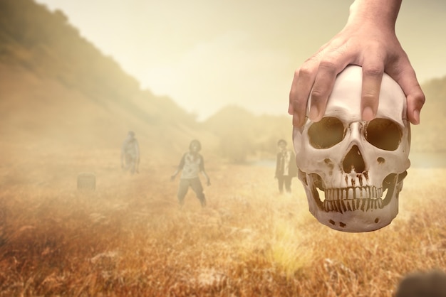 Main tenant un crâne humain sur le terrain avec des zombies ambulants en arrière-plan