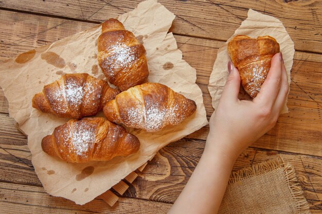 Photo main tenant un croissant croustillant frais français à partir d'une vue de dessus de table en bois