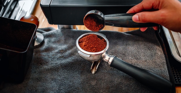 main tenant une cuillère versant du café broyeur de poudre broyant du café versant dans un porte-filtre