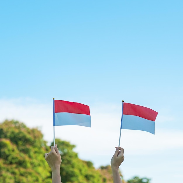 Main tenant le drapeau de l'Indonésie sur fond de ciel bleu Fête de l'indépendance de l'Indonésie Fête nationale et concepts de célébration heureuse