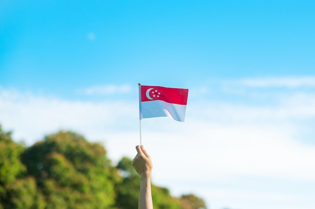 Main tenant le drapeau de Singapour sur fond de ciel bleu Fête nationale de Singapour et concepts de célébration heureuse