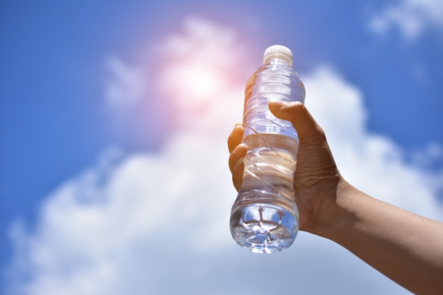 Main tenant l&#39;eau potable sur fond de nuages ​​ciel bleu