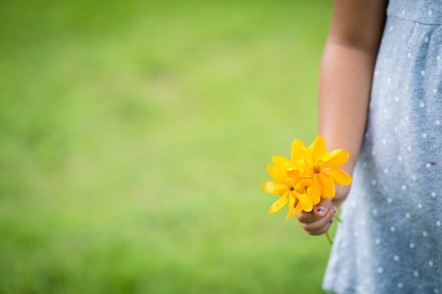 main tenant une fleur jaune sur fond de prairie