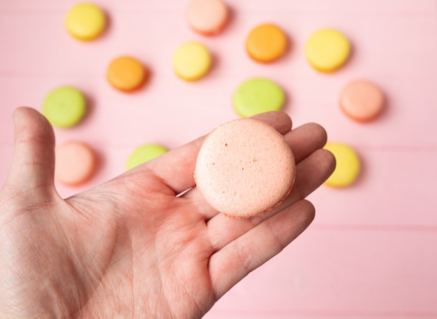 Main tenant des macarons français doux et colorés ou macaron sur table rose