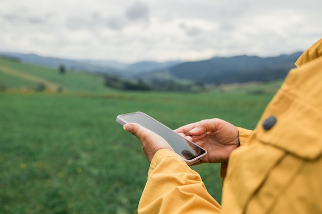 La main tenant et montrant un téléphone intelligent blanc en plein air avec des montagnes vertes floues en arrière-plan haut