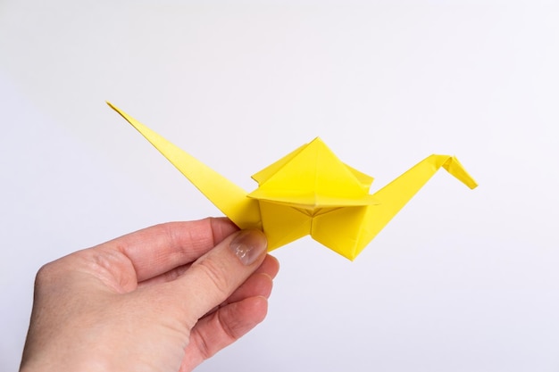 Une main tenant un oiseau jaune en papier sur un fond clair Grue en papier comme symbole de paix Origami en papier