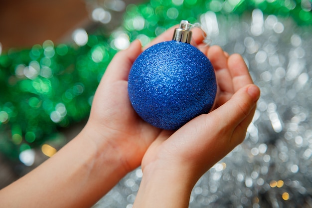 Main tenant l'ornement de boule bleue se bouchent la décoration de sapin de Noël à la maison sur fond brillant