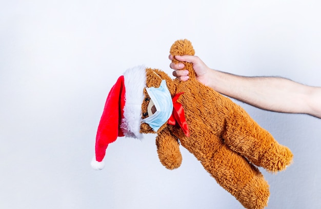Main tenant l'ours en peluche, avec masque et chapeau de père Noël, sur blanc